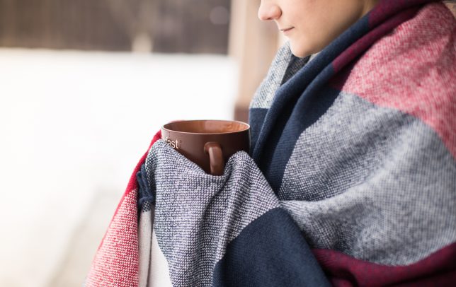 Girl in blanket drinks hot tea in winter